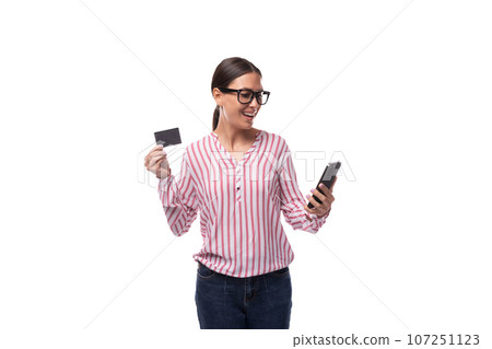 young well-groomed slender European leader woman with black hair holds a credit card and a mobile young well-groomed slender European leader woman with black hair holds a credit card and a mobile 107251123