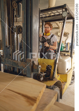 Male craftsman at wooden sawmill warehouse is loading with loader wooden board. High quality photo Male craftsman at wooden sawmill warehouse is loading with loader wooden board. High quality photo 107254590