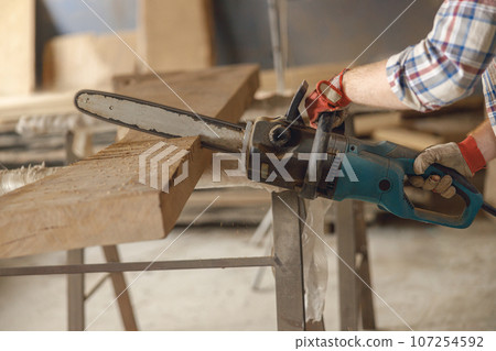 Close up of professional carpenter is cutting wood with chainsaw on carpentry workshop 107254592