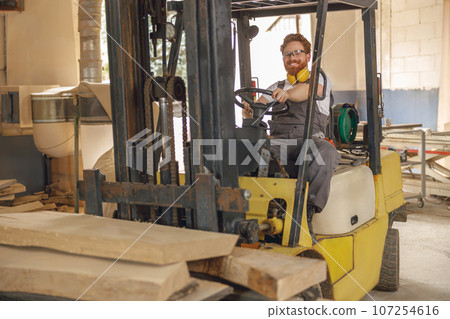 Male craftsman at wooden sawmill warehouse is loading with loader wooden board. High quality photo Male craftsman at wooden sawmill warehouse is loading with loader wooden board. High quality photo 107254616