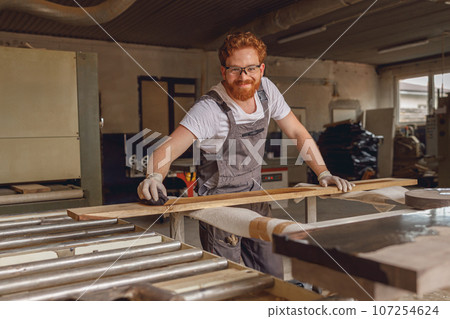 Craftsman coating a wooden board with protective oil in a workshop. Process of making a wood table 107254624