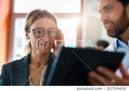 Close up of optometrist helping woman to choose glasses in optical store showing to her mirror Close up of optometrist helping woman to choose glasses in optical store showing to her mirror 107254630
