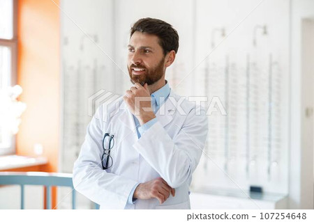 Portrait of smiling ophthalmologist in front of showcase in optics store looks away Portrait of smiling ophthalmologist in front of showcase in optics store looks away 107254648
