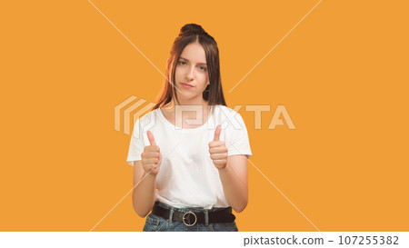 Sarcastic expression. Skeptic emotion. Disappointed doubtful woman with hands thumb up gesture sign isolated on orange background copy space. Sarcastic expression. Skeptic emotion. Disappointed doubtful woman with hands thumb up gesture sign isolated on orange background copy space. 107255382