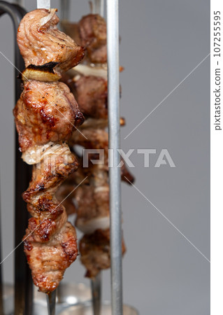 Cooking pork meat in an electric kebab maker on vertical skewers 107255595