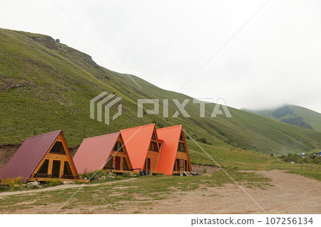 a-frame triangular houses in mountains, around rocks and green grass 107256134