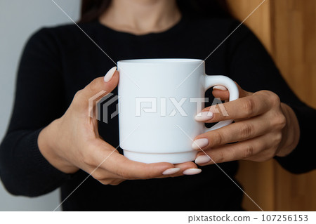 White mug for tea and coffee in the hands of a girl, close-up White mug for tea and coffee in the hands of a girl, close-up 107256153