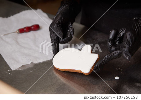 the cook holds a ready made cookie covered with white icing with his gloved hands 107256158