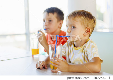 Cute children drinking soda or soft drink with straw in a fast food restaurant 107256201