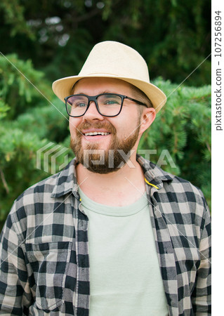 Laughing millennial man wearing hat over green tree background vertical - emotion and vacation travel holidays concept 107256894