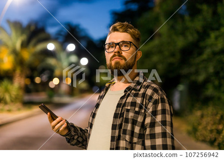 Millennial man waits taxi by using transportation app on night street. Technologies app and city concept 107256942
