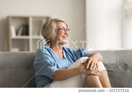 Positive blonde older mature woman sitting on home couch Positive blonde older mature woman sitting on home couch 107257528
