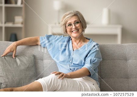 Happy mature old woman in glasses resting on soft couch Happy mature old woman in glasses resting on soft couch 107257529