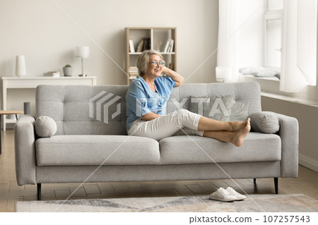 Cheerful dreamy senior pensioner woman relaxing on comfortable couch 107257543