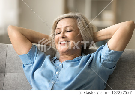 Positive calm senior retired woman resting on comfortable home sofa 107257557
