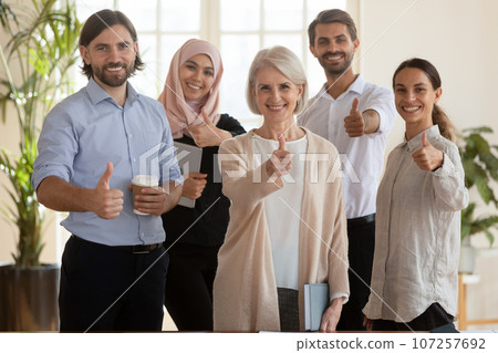 Five multicultural staff smiling showing thumbs up posing for camera 107257692