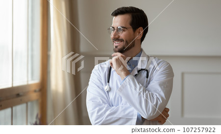 Smiling doctor wearing glasses standing in office, looking to aside 107257922