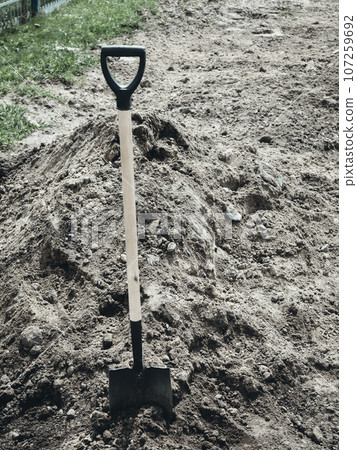 Shovel is stuck into pile of earth. Fresh grave or burial in cemetery. Background. Shovel is stuck into pile of earth. Fresh grave or burial in cemetery. Background. 107259692