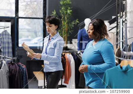African american customer asking store employee for help with elegant shoes, discussing fabric before buying it. Stylish woman shopping for fashionable clothes in modern boutique. Fashion concept 107259900