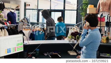 African american robber stealing basic shirt in modern boutique, being caught by asian security guard. Thief running from bodyguard, trying to escape the accusations. Crime concept 107259921