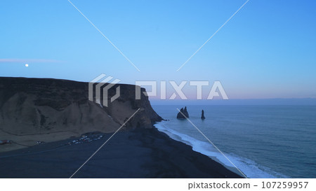 Drone shot of black sand beach with rocks and massive hills in iceland, majestic natural landscape on reynisfjara beach. Icelandic scenery with frozen cliffs and lands, atlantic ocean. Slow motion. Drone shot of black sand beach with rocks and massive hills in iceland, majestic natural landscape on reynisfjara beach. Icelandic scenery with frozen cliffs and lands, atlantic ocean. Slow motion. 107259957