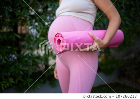 a young pregnant woman holds a pink yoga mat in her hands. close-up shot 107260218