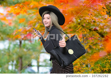 A female traveler taking pictures of autumn leaves with a smartphone 107262282