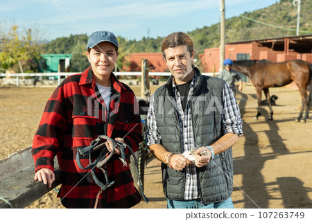 Portrait of two male female grooms posing on yard of horse riding club Portrait of two male female grooms posing on yard of horse riding club 107263749