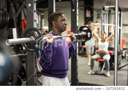 African american man doing barbell squats in gym 107263832