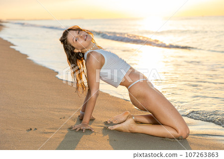 Woman in strings with perfect body kneeling on beach Woman in strings with perfect body kneeling on beach 107263863