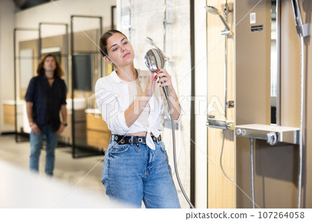Positive young woman choosing a shower head in hardware store Positive young woman choosing a shower head in hardware store 107264058