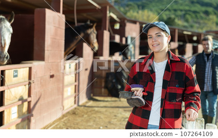 Cheerful female holding brushes for grooming horses outdoors 107264109