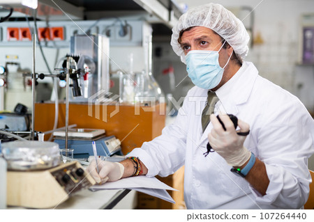 Male scientist engaged in research in chemical laboratory, noting results in chart 107264440