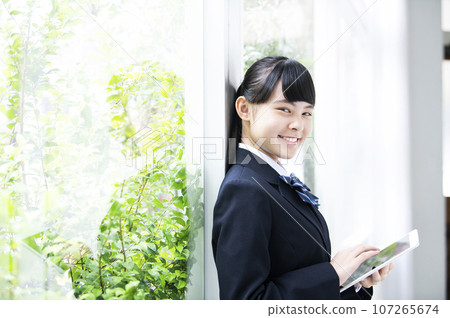 Junior high school girl holding a tablet by the window, looking at the camera 107265674