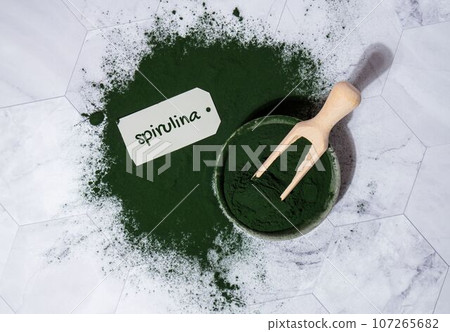 Blue-green algae Chlorella and spirulina powder in bowl with paper note text SPIRULINA. Super powder. Natural supplement of algae. Detox superfood drink cocktail. Food supplement source of protein and Blue-green algae Chlorella and spirulina powder in bowl with paper note text SPIRULINA. Super powder. Natural supplement of algae. Detox superfood drink cocktail. Food supplement source of protein and 107265682