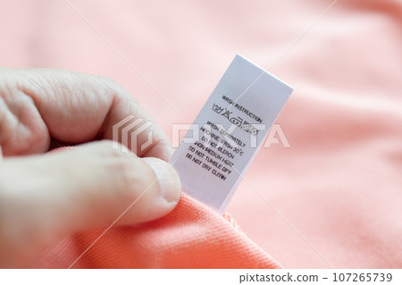 Hand hold and reading at white laundry care washing instructions clothes label on pink shirt Hand hold and reading at white laundry care washing instructions clothes label on pink shirt 107265739