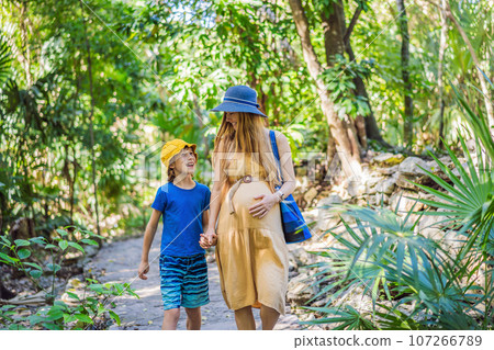 Expectant mother and her son enjoying a leisurely stroll in the park, cherishing precious moments amidst nature's beauty Expectant mother and her son enjoying a leisurely stroll in the park, cherishing precious moments amidst nature's beauty 107266789