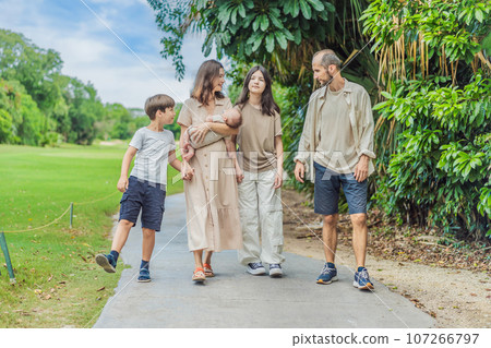 Happy couple in their 40s, surrounded by adult children, cradle a newborn in a sunlit park. Love, family, and generations in harmony 107266797