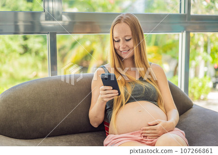 Mobile pregnancy online maternity application. Pregnant mother using phone. Pregnancy, medicine, pharmaceutics, health care and people concept Mobile pregnancy online maternity application. Pregnant mother using phone. Pregnancy, medicine, pharmaceutics, health care and people concept 107266861