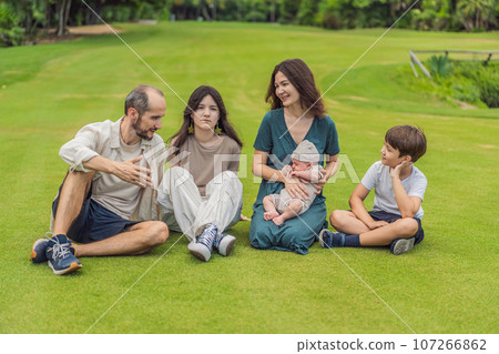 Happy couple in their 40s, surrounded by adult children, cradle a newborn in a sunlit park. Love, family, and generations in harmony 107266862