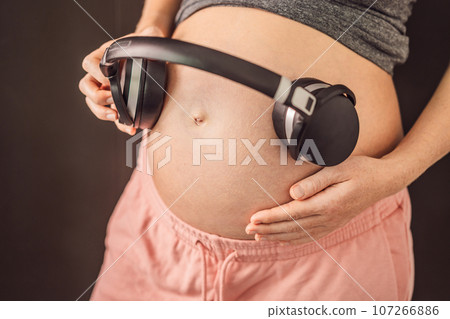 Melodies in the womb: Headphones placed on a pregnant belly, bonding through music, a heartwarming connection between mother and baby 107266886