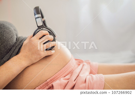 Melodies in the womb: Headphones placed on a pregnant belly, bonding through music, a heartwarming connection between mother and baby Melodies in the womb: Headphones placed on a pregnant belly, bonding through music, a heartwarming connection between mother and baby 107266902