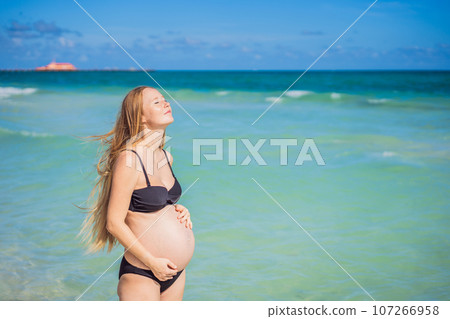 Radiant pregnant woman in a swimsuit, amid the stunning backdrop of a turquoise sea. Serene beauty of maternity by the shore Radiant pregnant woman in a swimsuit, amid the stunning backdrop of a turquoise sea. Serene beauty of maternity by the shore 107266958