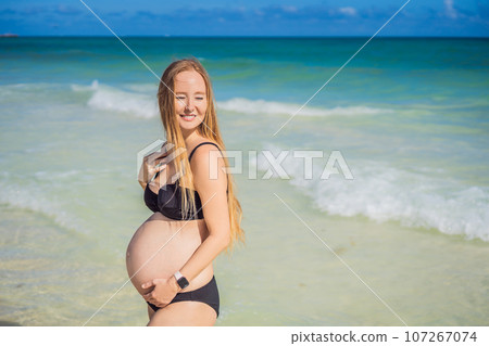Radiant pregnant woman in a swimsuit, amid the stunning backdrop of a turquoise sea. Serene beauty of maternity by the shore Radiant pregnant woman in a swimsuit, amid the stunning backdrop of a turquoise sea. Serene beauty of maternity by the shore 107267074