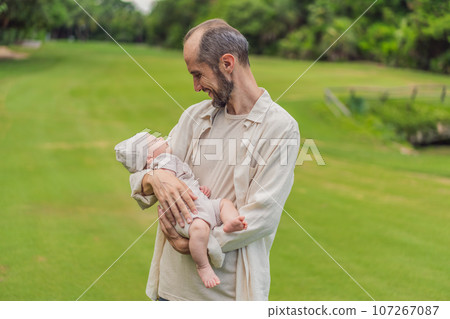 A happy 40-year-old father cradles her newborn in a sun-drenched park. Love, family and generations in harmony 107267087
