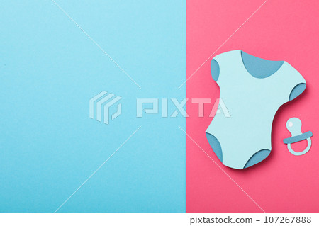 Paper baby clothes and pacifier on blue and pink background, space for text 107267888
