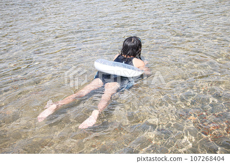 Image of a girl playing in the water with a float and designated swimsuit Image of a girl playing in the water with a float and designated swimsuit 107268404