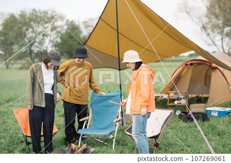 Outdoor image of young men and women enjoying camping and making a bonfire 107269061