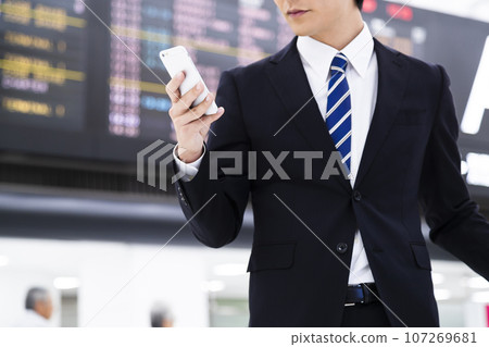 Young businessman on a business trip from the airport while looking at his smartphone 107269681