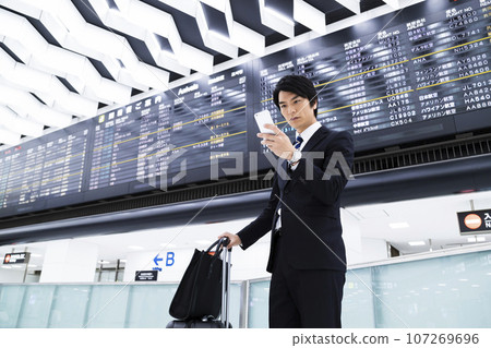 Young businessman on a business trip from the airport while looking at his smartphone 107269696